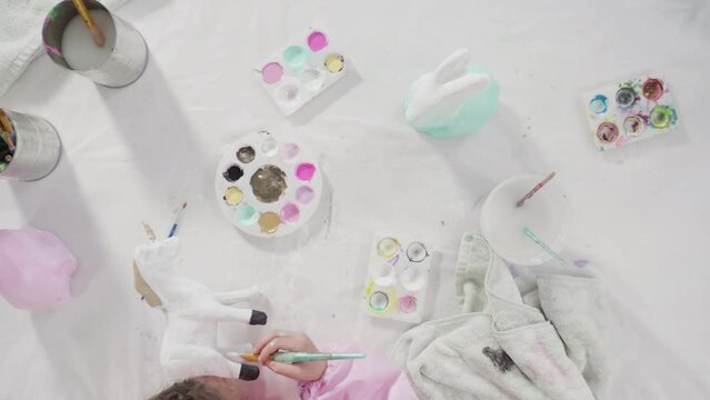 Flat lay. Little girl painting paper mache figurine at homeschooling art class.
