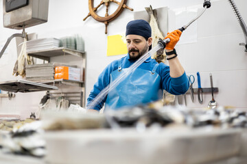 A middle-aged fishmonger in an apron is dousing produce with water from a hose, selling food, small and medium-sized business.