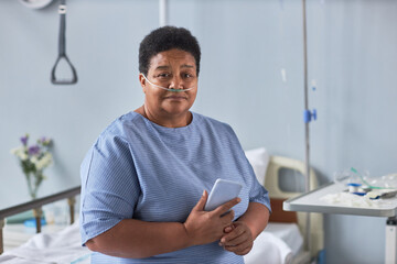 Portrait of black senior woman sitting on bed in hospital room with oxygen cannulas