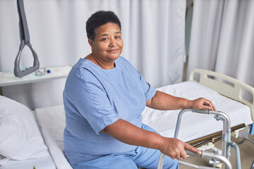 Portrait of African American senior woman looking at camera while sitting on bed in hospital room