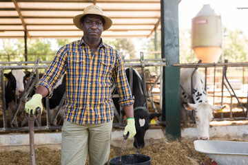 Portrait of cheerful afro american male farmer who is standing at the cow farm