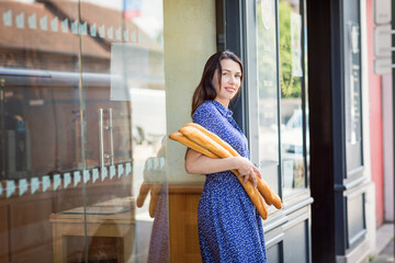 Young pretty woman buying a french baguette and standing on the street in city