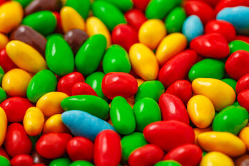 Candy in multi colored glaze in bulk, grains kernels seeds, uniform texture pattern, wallpaper background, selective focus