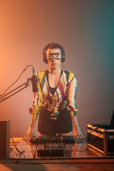Female DJ standing at turntables and mixing equipment, using audio instruments or mixer to perform...