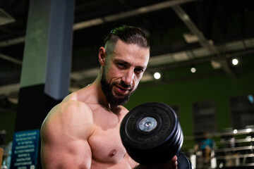 Fototapeta na wymiar A handsome muscular male bodybuilder with a beard does a biceps exercise with a dumbbell