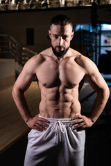 Fototapeta na wymiar A handsome muscular male bodybuilder with a pumped-up torso with a beard and white pants looks at the camera