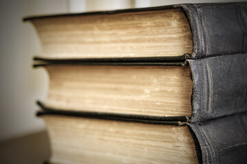 Old books are stacked close-up, binding black covers, selective focus, side view
