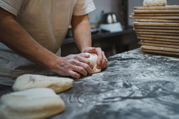 Baker kneading bread dough on messy counter full of flour in bakery