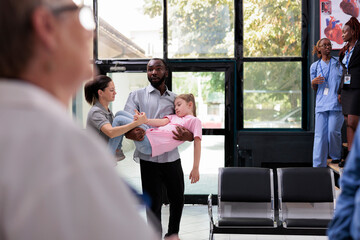 Worried african american dad holding unconscious little daughter in arms after fainting while bringing little girl in hospital waiting room asking medical staff for help. Health care service