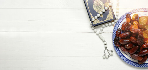 Plate with dates, Quran book and prayer beads on white wooden background with space for text