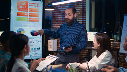 Company financial analyst speaking in business meeting presentation, holding digital tablet. Diverse office workers team discussing revenue statistics, looking at graphs on screen