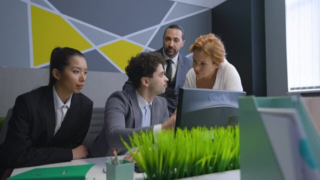 Employees, colleagues in the office gathered at the computer, discuss the document, solve work issues.