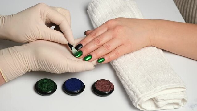 Manicurist rubbing in green chrome powder on black nails. Trendy nail art design with shiny metallic cover. Metal chrome nails