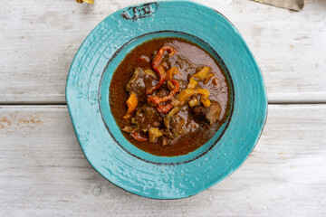 Gulasch mit Paprika in Teller und auf Holztisch 