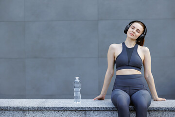 Relaxed woman in activewear listening to music, resting after workout outdoors.