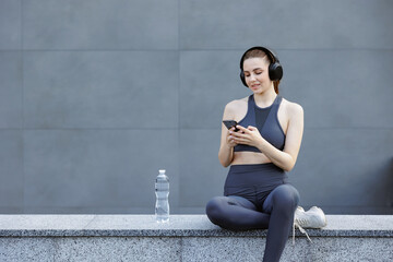 Beautiful sportswoman browsing internet on smartphone, while resting outside.