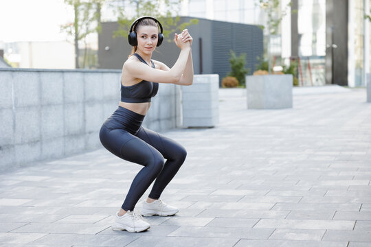 Determined Athletic Girl Listening Music, Squatting During Workout In City.