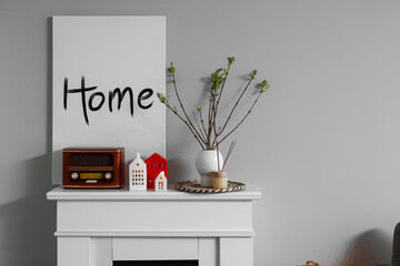 Vase with tree branches, house candle holders and retro radio receiver on fireplace near grey wall