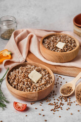 Wooden bowls of tasty buckwheat porridge with butter and vegetables on grey table