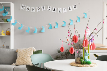 Vase with tree branches, Easter eggs, candles and rabbits on table in kitchen