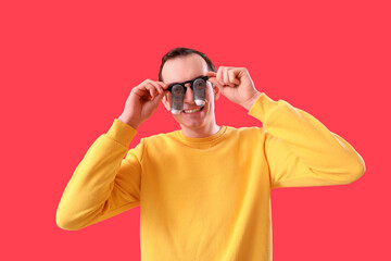 Young man in funny eyeglasses on red background. April Fools' Day celebration