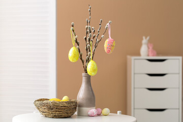 Vase with willow branches and beautiful Easter eggs on table in room