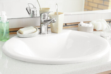Table with white ceramic sink and bath supplies in room, closeup
