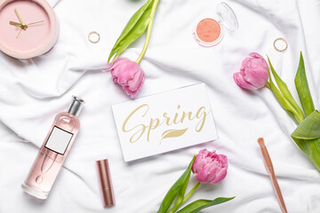 Composition with cosmetics, tulip flowers, alarm clock and card on light fabric background
