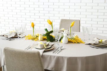 Festive dining table served for Easter celebration near white brick wall