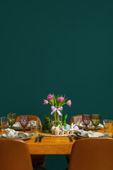 Festive dining table with painted eggs and tulip flowers served for Easter celebration near green wall