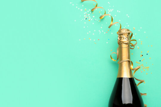 Bottle of champagne, serpentine and sequins on turquoise background