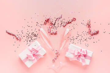 Champagne glasses, gift boxes, serpentine and sequins on pink background