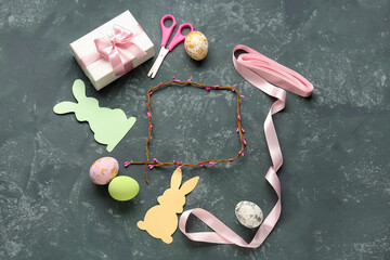 Frame made of tree branch, Easter eggs, paper rabbits, gift, scissors and ribbon on dark background