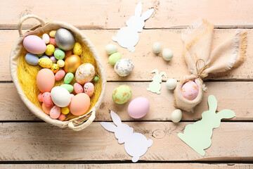 Obraz na płótnie Canvas Basket with Easter eggs and paper rabbits on beige wooden background
