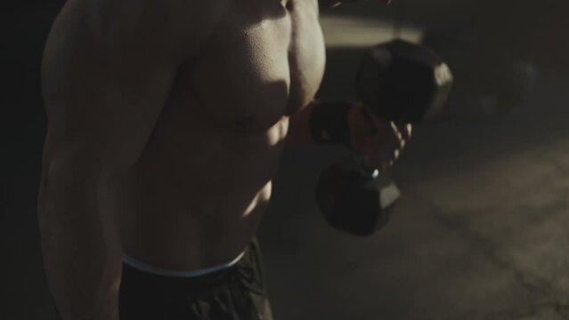 Athletic shirtless young sports man doing exercises with dumbbell in gym. Handsome men pumping up biceps muscle. close-up