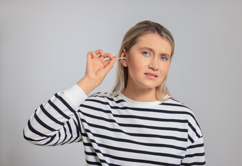 Young woman cleaning ear with cotton swab on light grey background