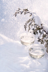 Two crystal glasses of sparkling wine or champagne cooling in snow on winter natural background with beautiful sunlight bokeh. Minimal creative composition with copy space. Holiday celebration concept