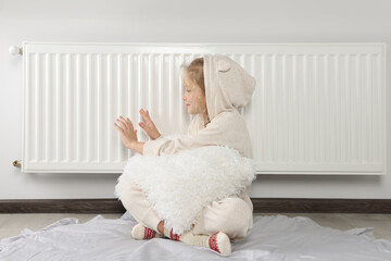Little girl warming hands near heating radiator indoors