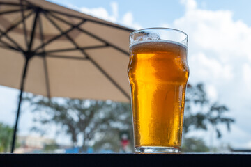 A clear pint drinking glass filled with cold froth from a lager ale. The Irish red ale pint sits on...