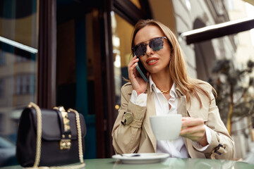 Fototapeta na wymiar Woman sitting at cafe terrace talking on phone while drinking coffee. High quality photo