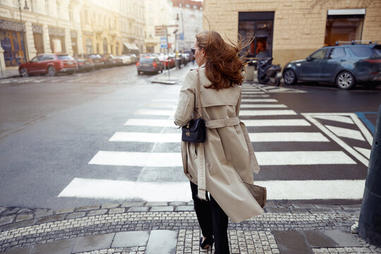 Woman in trendy outfits crosses road against backdrop of city buildings. High quality photo