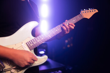 A man playing electric guitar close up on a concert stage. 