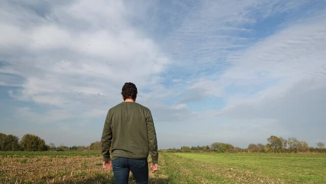 A young man walking into a field in a sunny day. Male model with a green sweater walking through a flat field in the center of the shot, Realizing that he has forgotten something, he turns to go back.