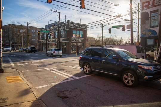 A Shot Of A Street With Cars And Trucks Driving, Powerlines, Bare Winter Trees, Shops And Restaurants With Cars Driving On The Street, Blue Sky And Clouds In Atlanta Georgia USA