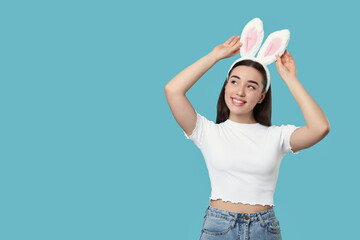 Happy woman wearing bunny ears headband on turquoise background, space for text. Easter celebration