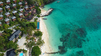 Aerial view of beautiful wooden bungalows in tropical rainforest overlooking white sand beach and...