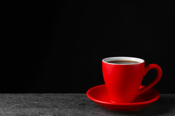 Red cup with aromatic coffee on grey textured table against black background. Space for text