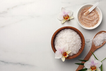 Flat lay composition with different spa products and flowers on white marble table. Space for text