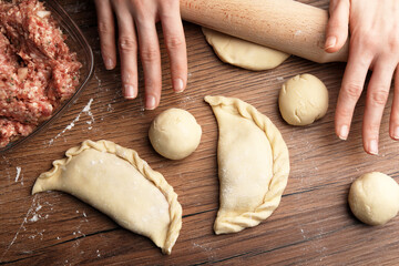 Woman rolling dough for chebureki on wooden table, flat lay