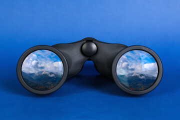 Binoculars on blue background. Mountain landscape reflecting in lenses